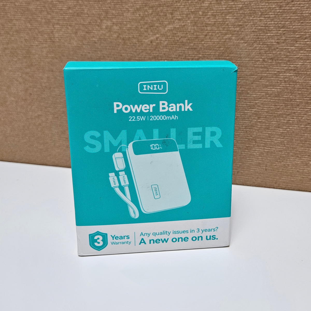 A boxed INIU Power Bank product package standing upright on a white surface against a brown textured backdrop.