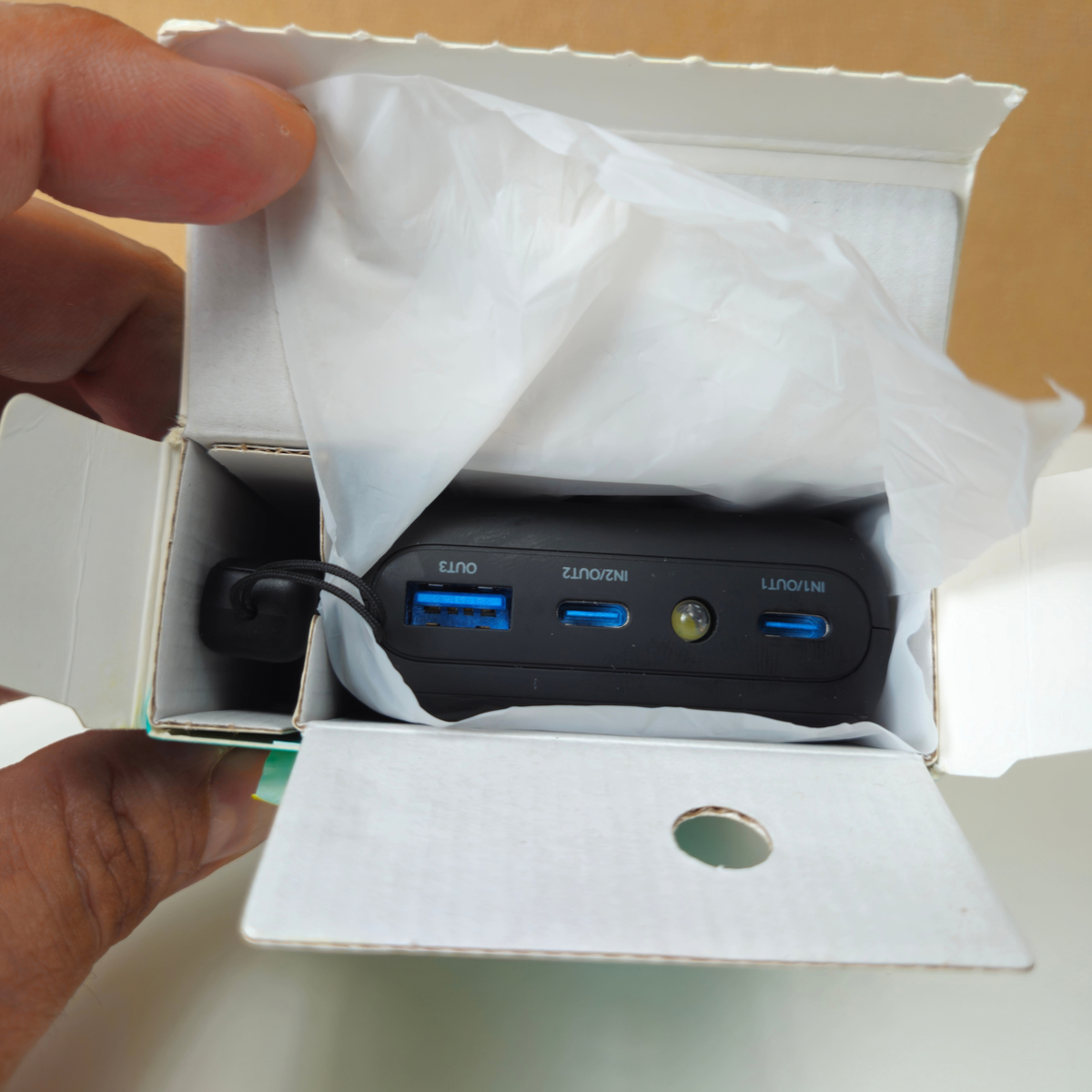 A black multi-port USB charger with blue ports, partially pulled from its white cardboard box with tissue paper.