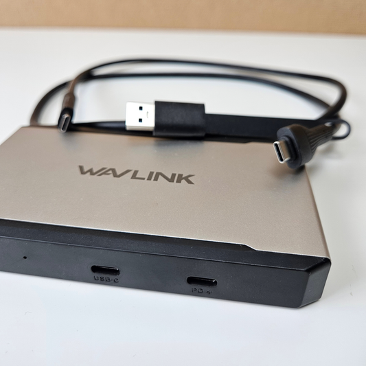 A silver and black Wavlink USB-C hub with a coiled black USB-C cable, photographed on a white surface with a beige background.