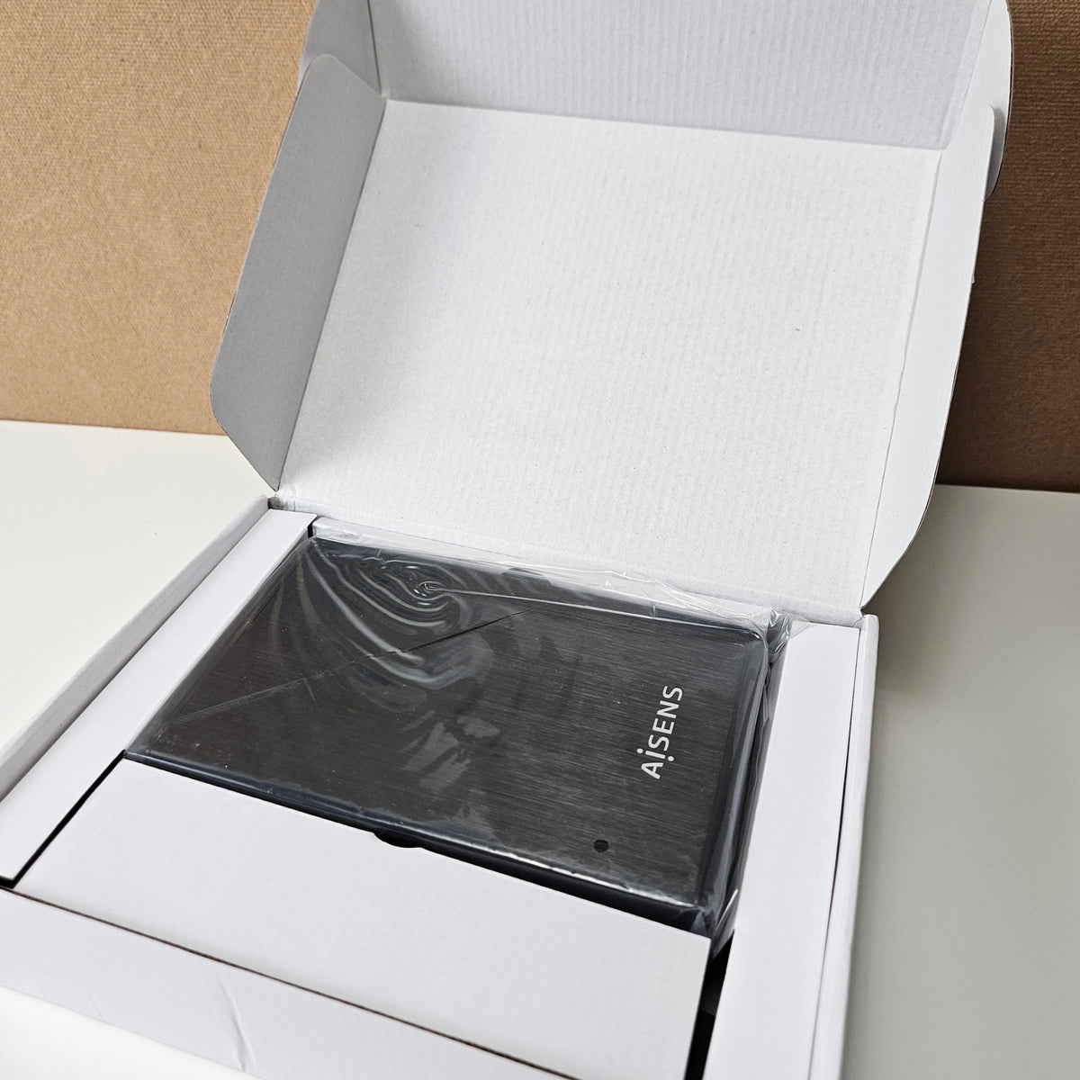 Black AISENS hard drive enclosure resting inside its white protective cardboard packaging