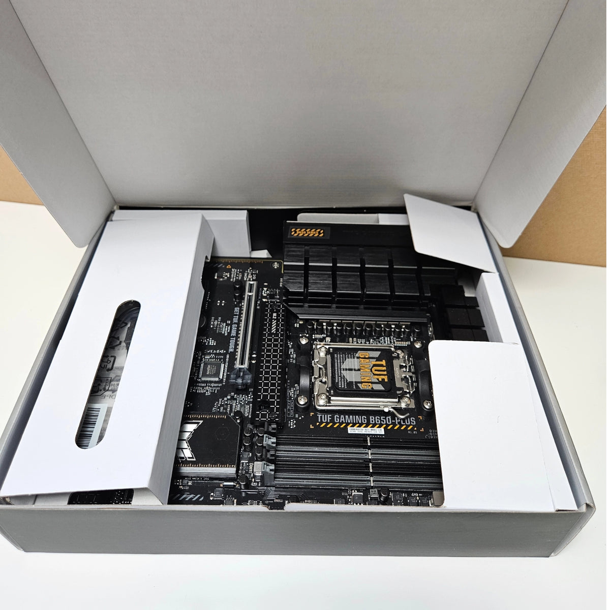 The ASUS TUF Gaming B650-PLUS motherboard resting inside its protective cardboard packaging