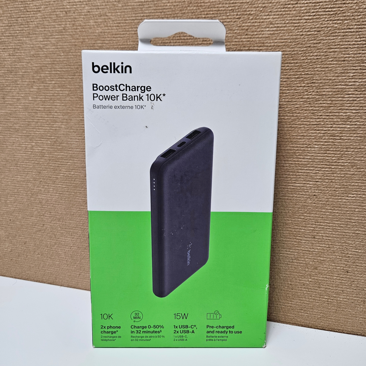 Belkin BoostCharge Power Bank 10K retail packaging box, showing the black power bank pictured on the front, photographed against a brown cardboard backdrop.