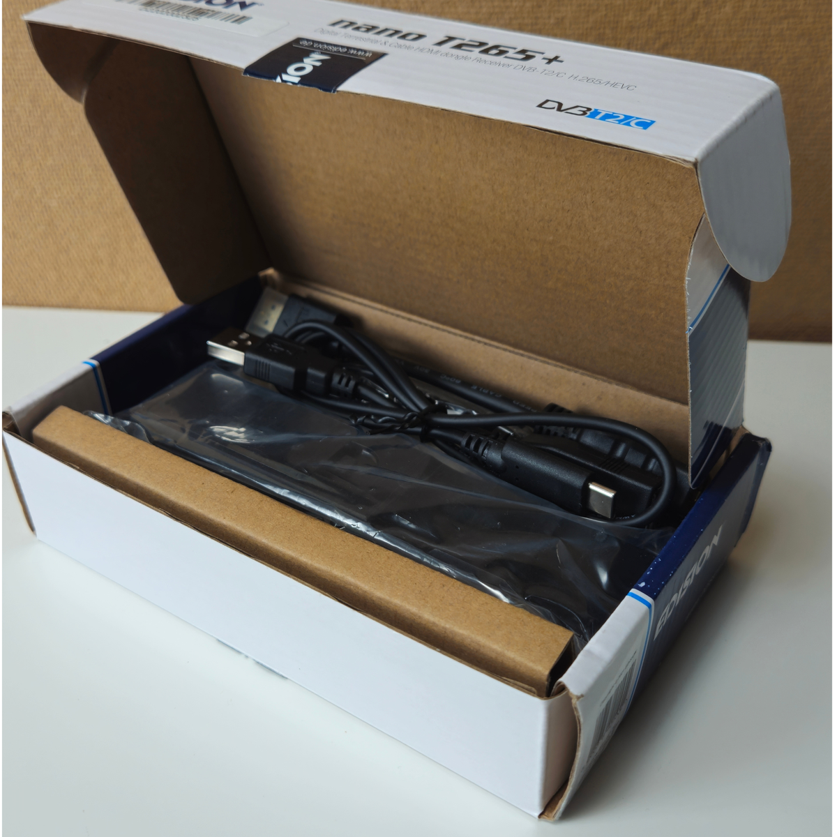 An open white and brown cardboard product box containing a black USB cable wrapped in protective plastic