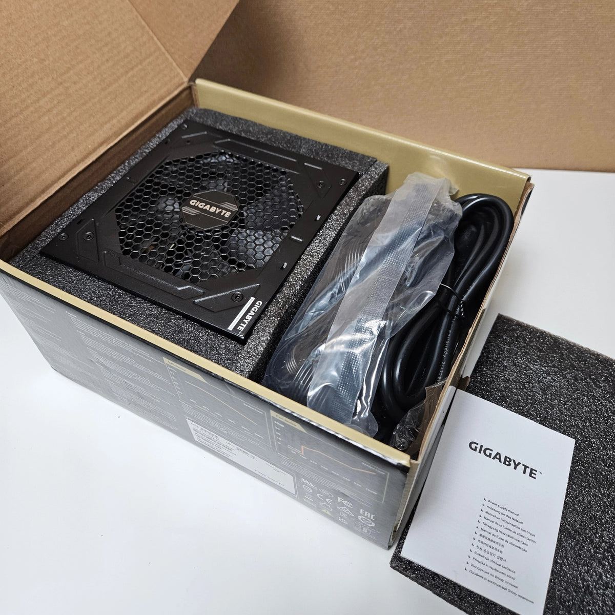 Open retail box revealing the Gigabyte P750GM power supply unit, manual, and packaged cables