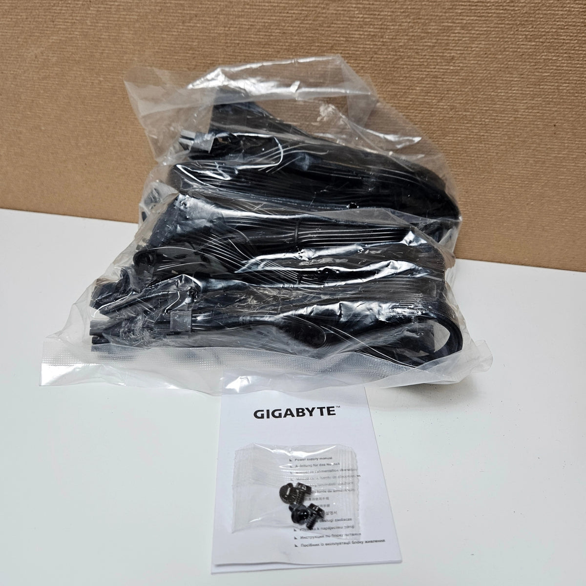 Sealed plastic pack of modular cables and mounting screws next to a Gigabyte user guide