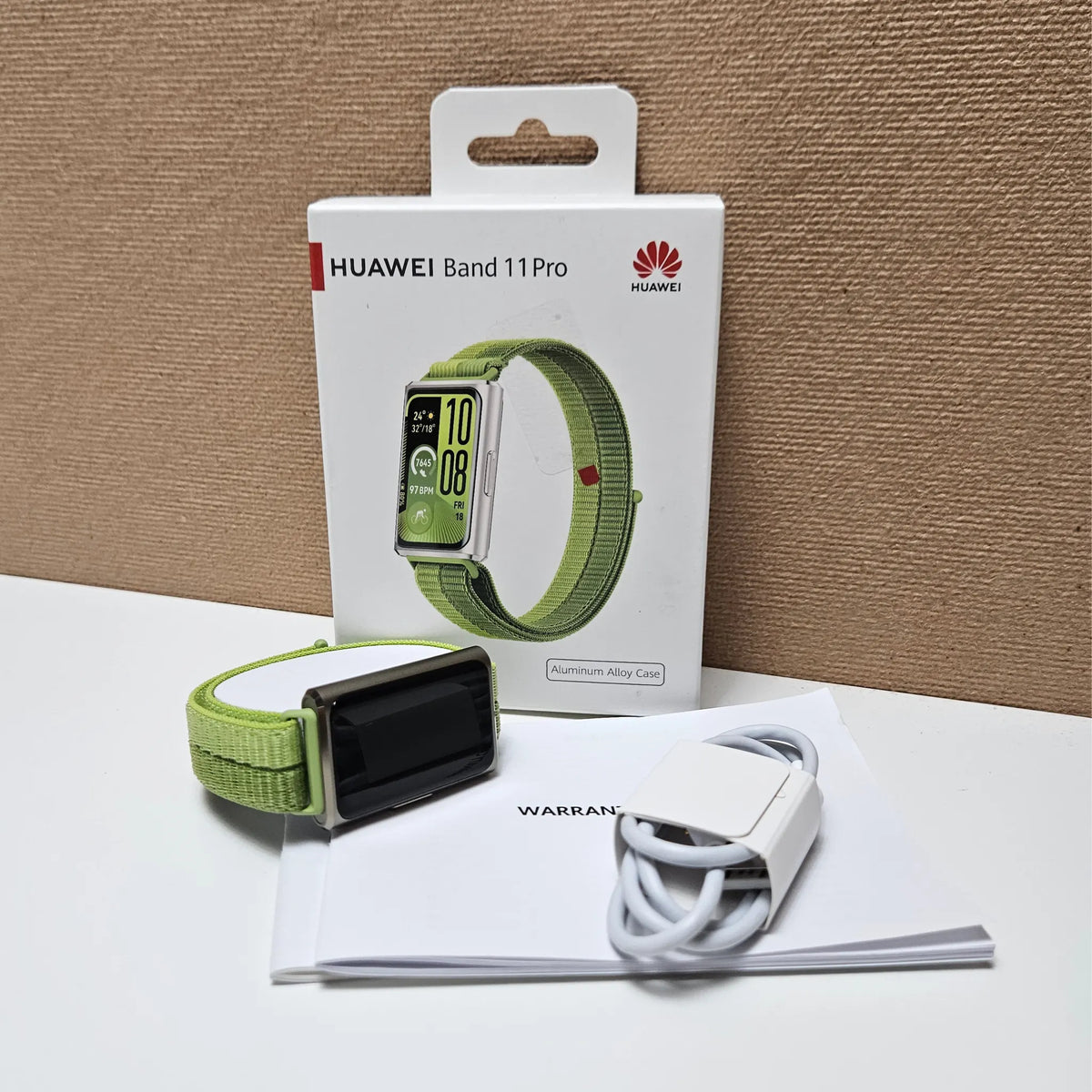 Huawei Band 11 Pro with green strap beside its retail box, white charging cable and printed documents.