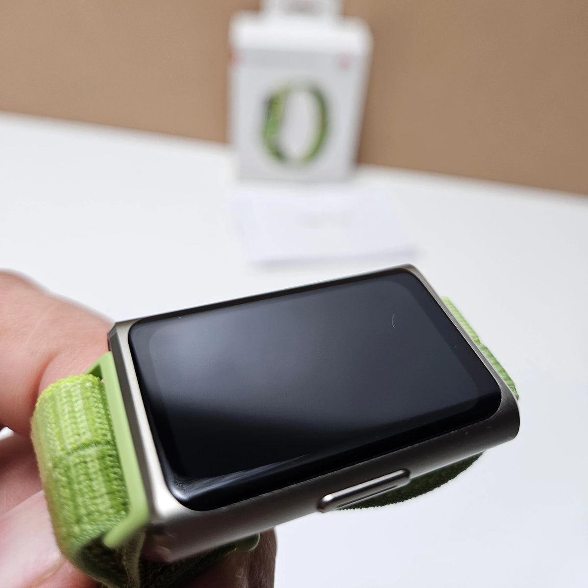 Angled close-up of Huawei Band 11 Pro showing the dark display, side button and green strap.