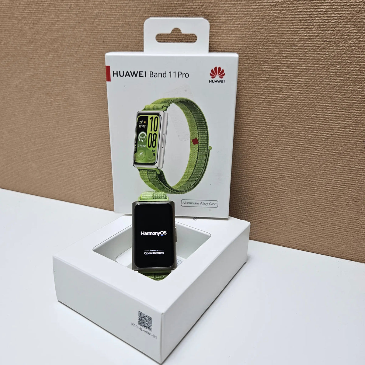 Huawei Band 11 Pro standing in its open packaging with the HarmonyOS startup screen visible.