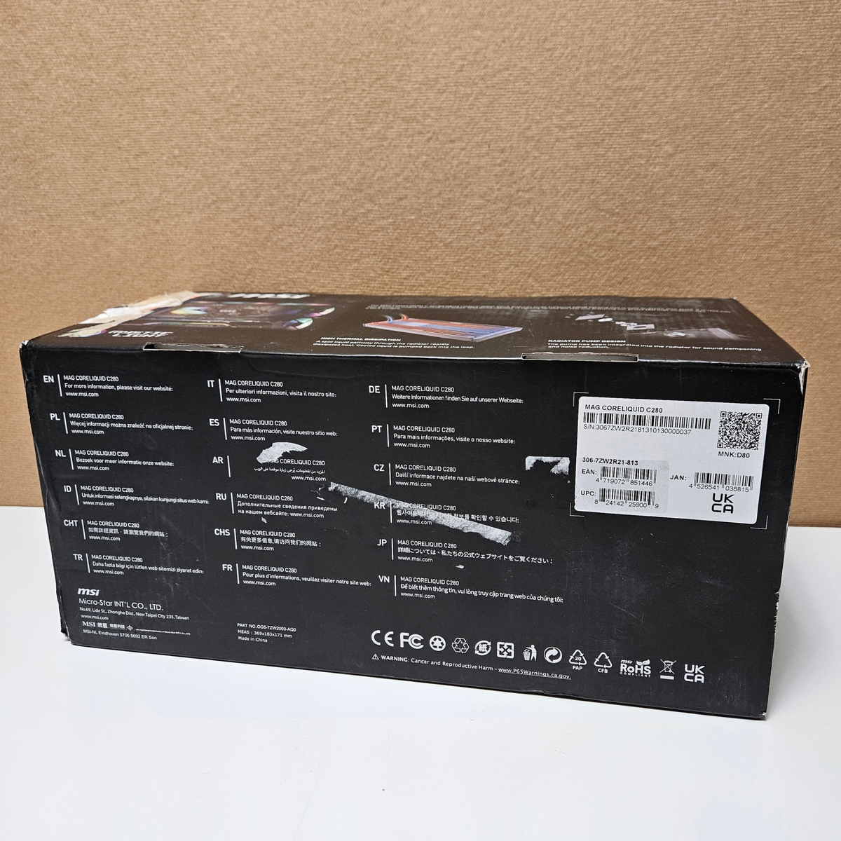 The back of a black retail box for a Msi  featuring technical specifications, regulatory icons, and a barcode sticker on a light surface against a brown cardboard background.