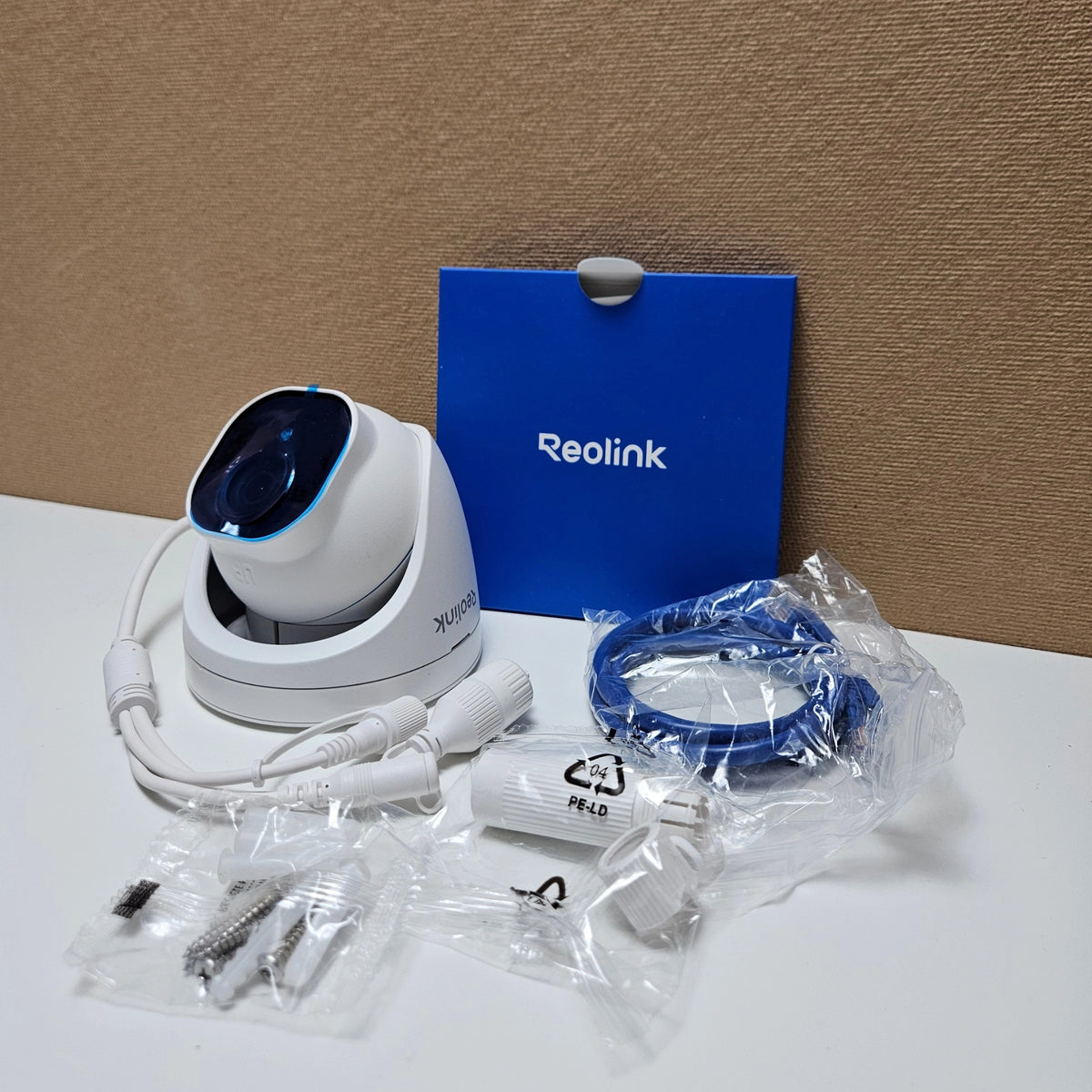 White Reolink dome camera displayed with included mounting screws, network cable, and manual.