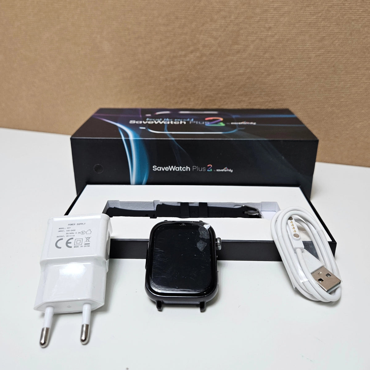 SaveFamily smartwatch body displayed with its charging cable and adapter