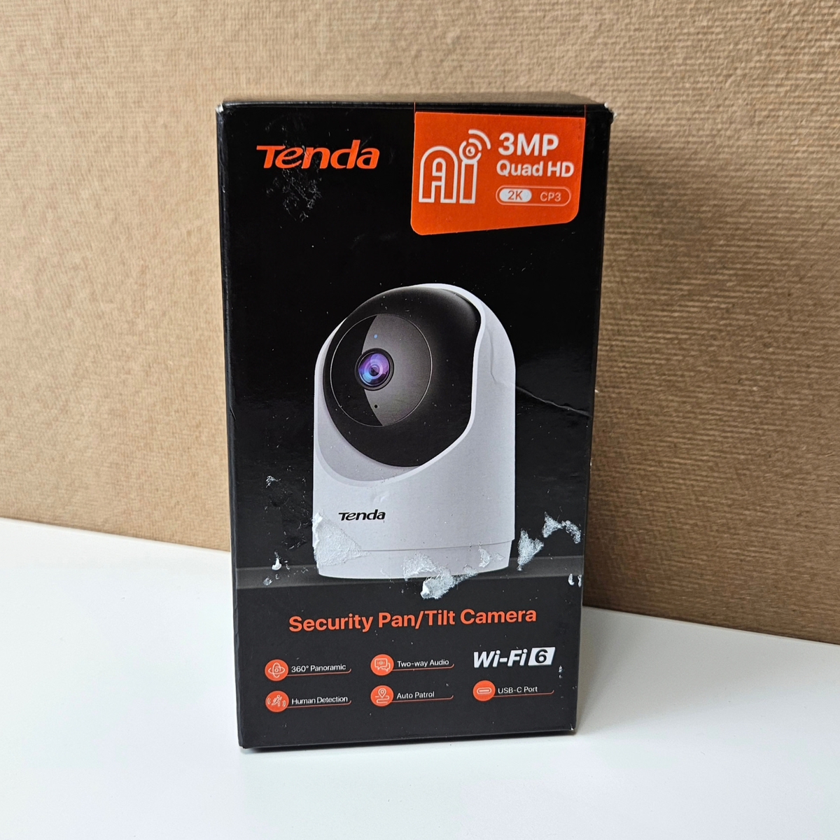 Tenda 3MP Quad HD security pan/tilt camera retail box, featuring a black and orange design with a graphic of the white and black camera, set against a brown cardboard backdrop.