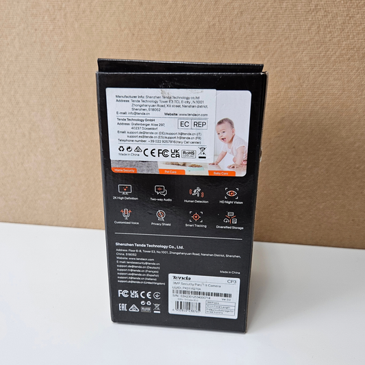 The back of a black retail box, showing technical specifications, icons, and a small photo of a baby, standing on a white surface against a beige textured background.