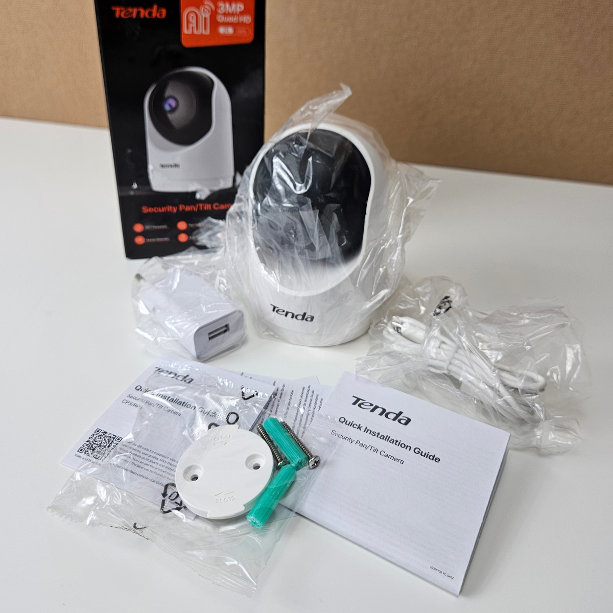 Tenda Security Camera showing the spherical white device alongside its original box, a USB power adapter, a charging cable, mounting screws, and a printed quick installation guide.