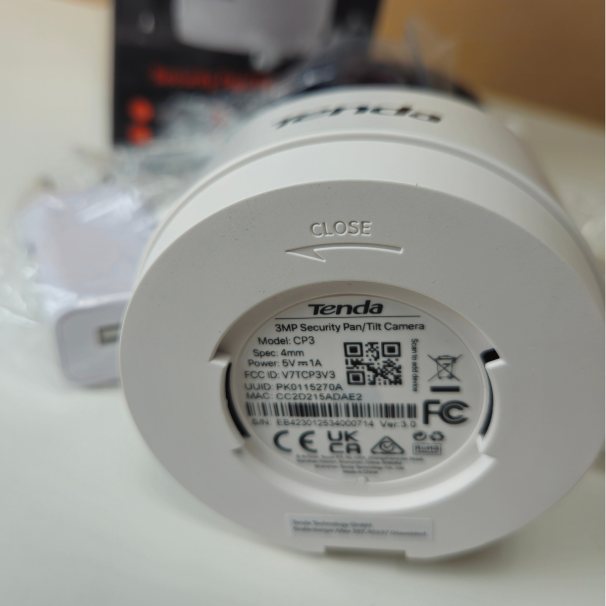 A Tenda 3MP Security Pan/Tilt Camera shown from the bottom, displaying its white plastic casing and printed specifications on the underside.
