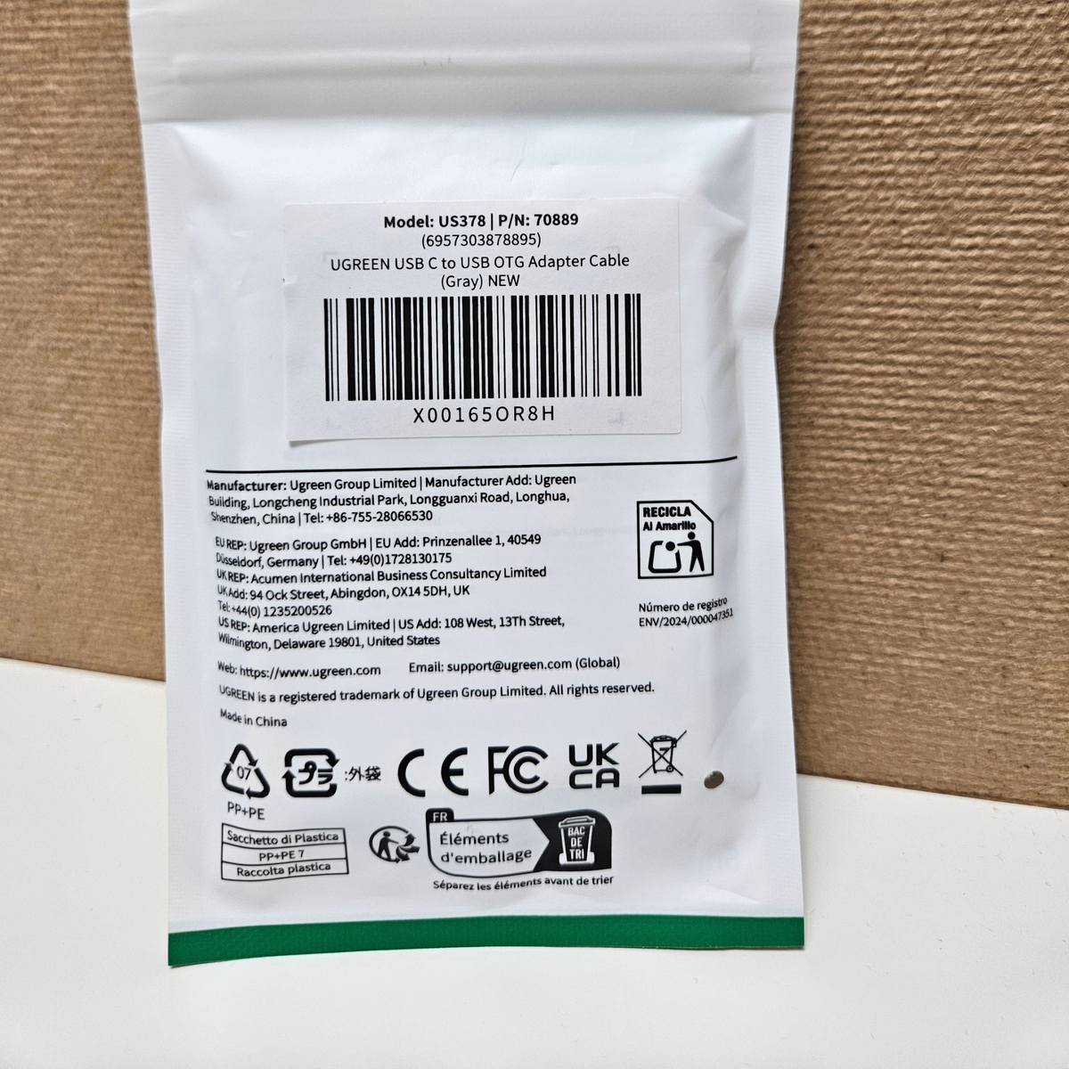 Back of a UGREEN USB-C to USB OTG adapter cable packaging, showing a barcode, product model, manufacturer details, and compliance logos on a white pouch with a green stripe.
