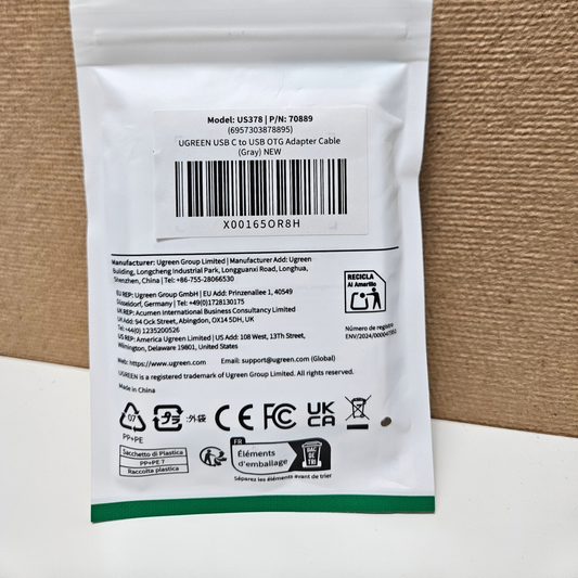 Back of a UGREEN USB-C to USB OTG adapter cable packaging, showing a barcode, product model, manufacturer details, and compliance logos on a white pouch with a green stripe.