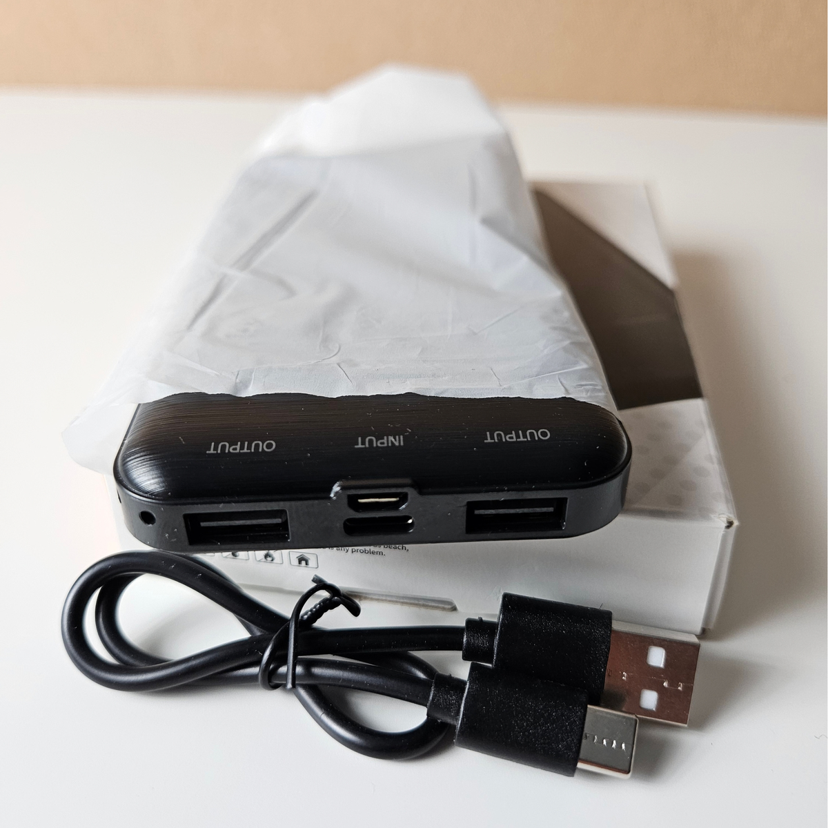 A black multi-port USB hub with labeled OUTPUT and INPUT ports, shown with a black USB cable in front of its white retail box on a light surface.